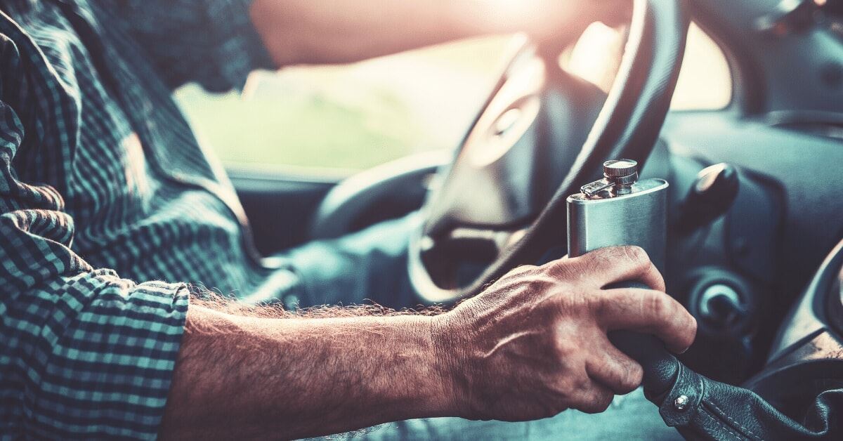 man holding alcohol flask while driving